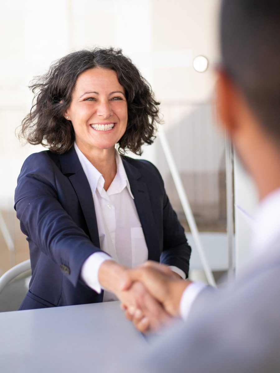 Happy successful business colleagues meeting outside and closing deal. Joyful business woman and man sitting at table, talking and shaking hands. Closing deal concept